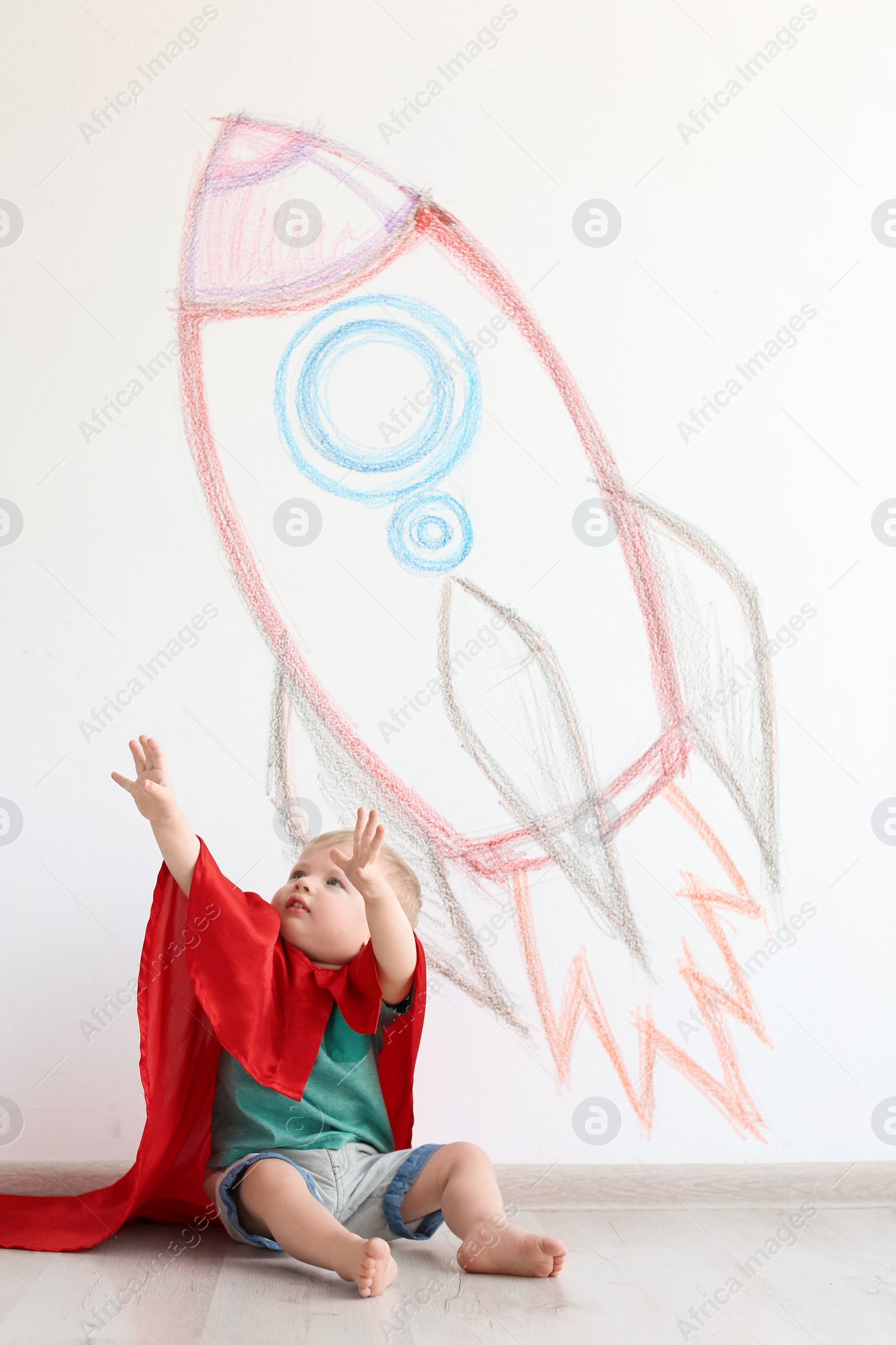 Photo of Adorable little child playing astronaut near wall with drawing of spaceship indoors