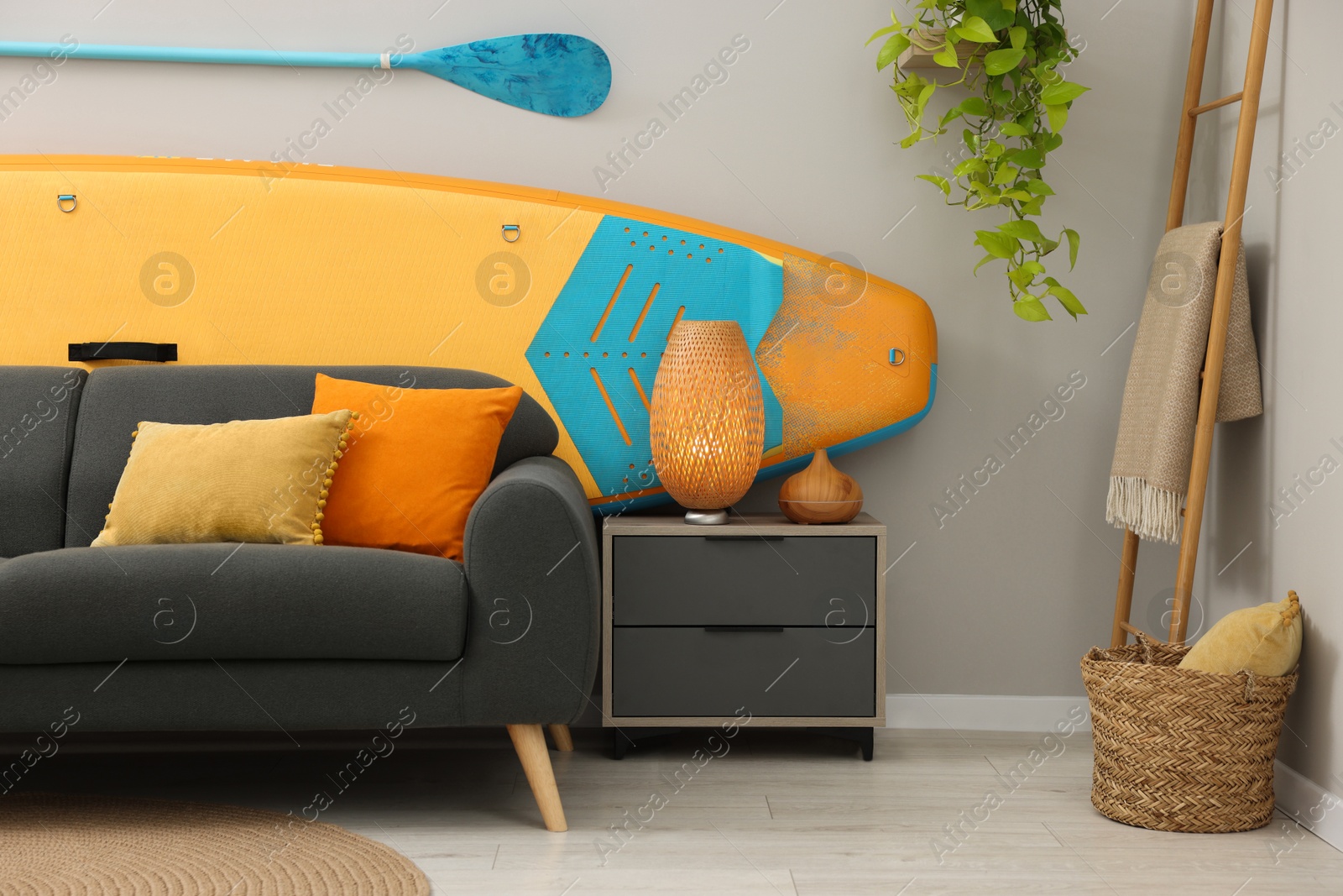 Photo of SUP board, paddle and stylish sofa in living room. Interior design