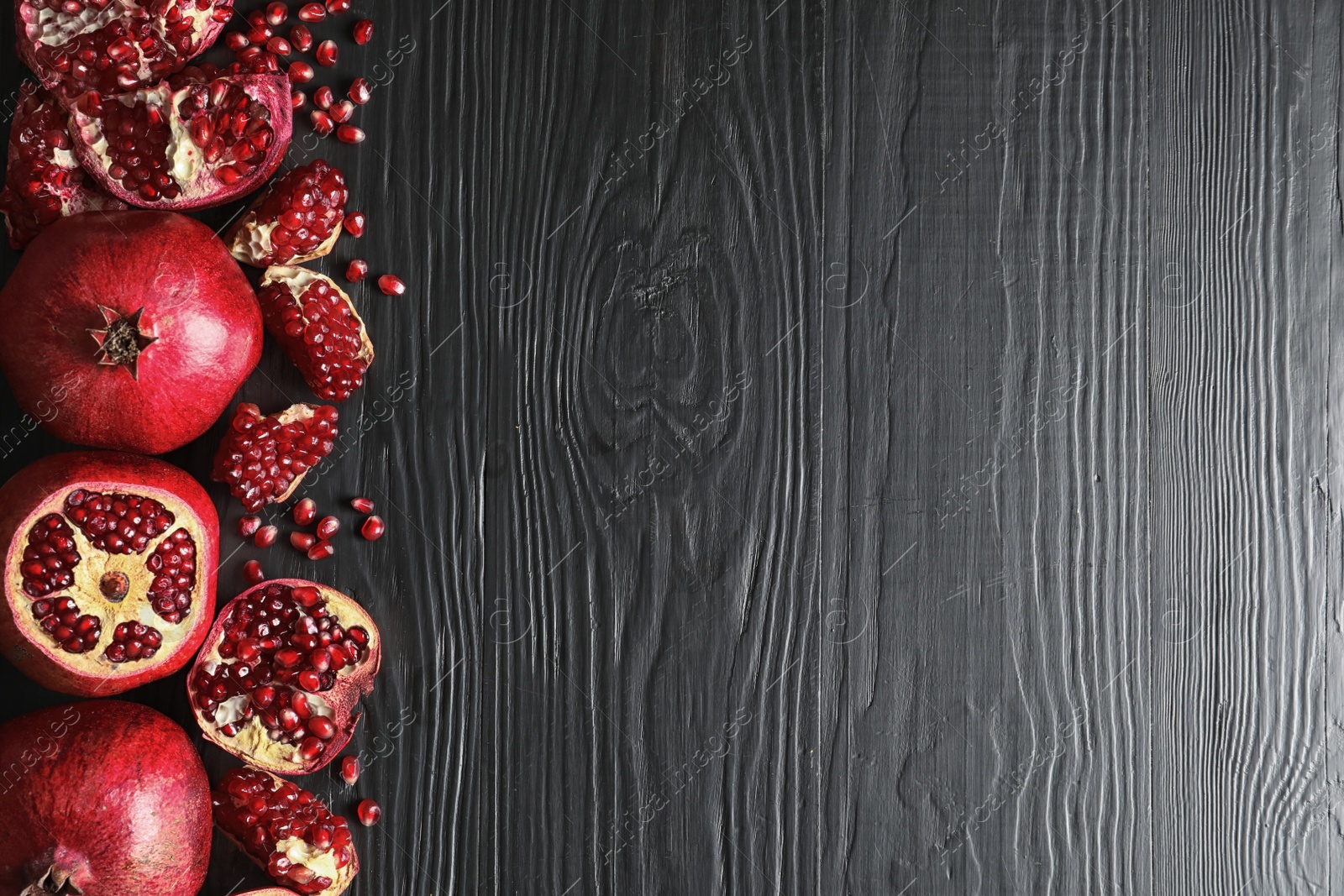 Photo of Ripe pomegranates on dark wooden background, top view with space for text