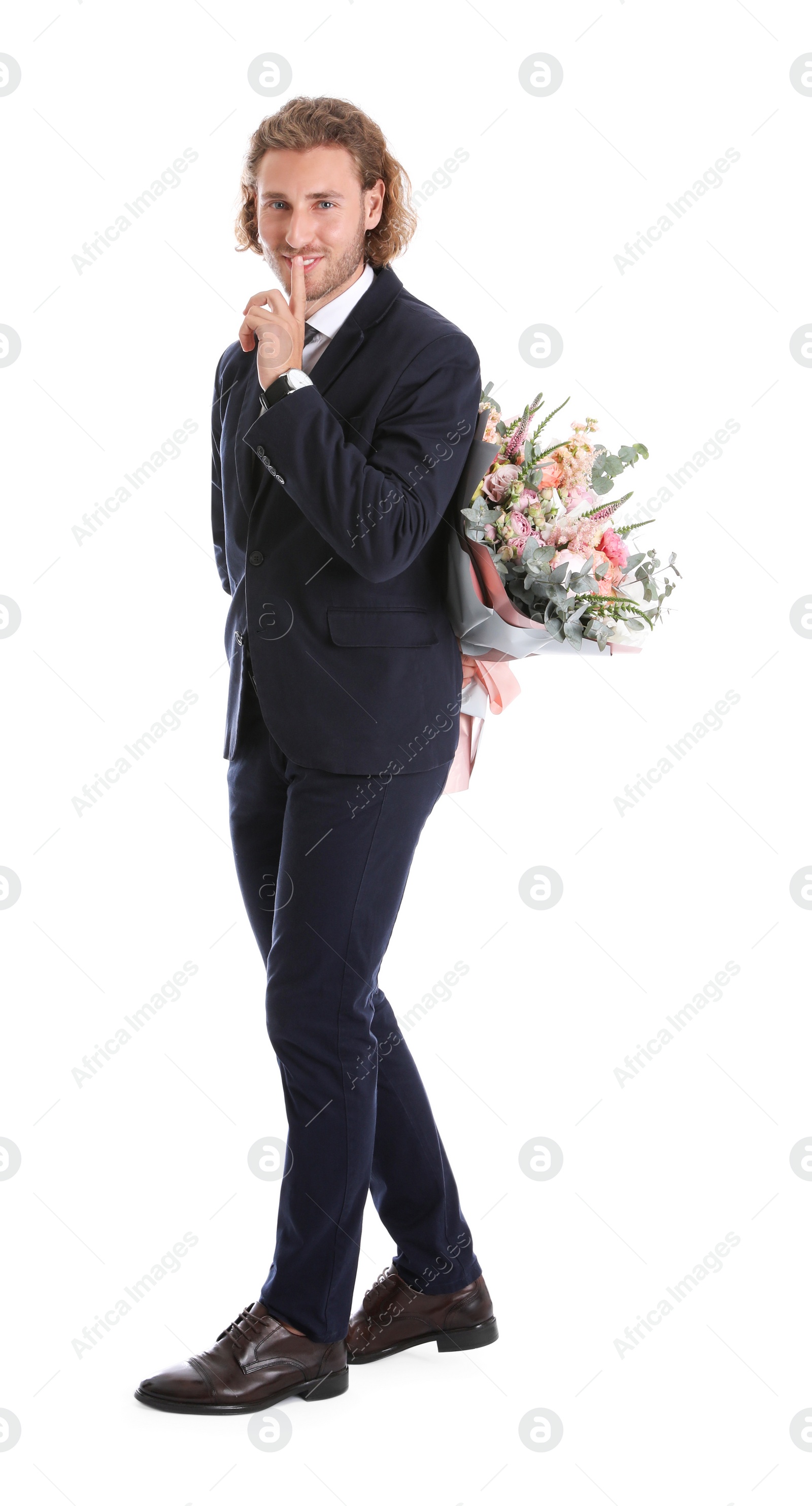 Photo of Young handsome man in stylish suit hiding beautiful flower bouquet behind his back on white background