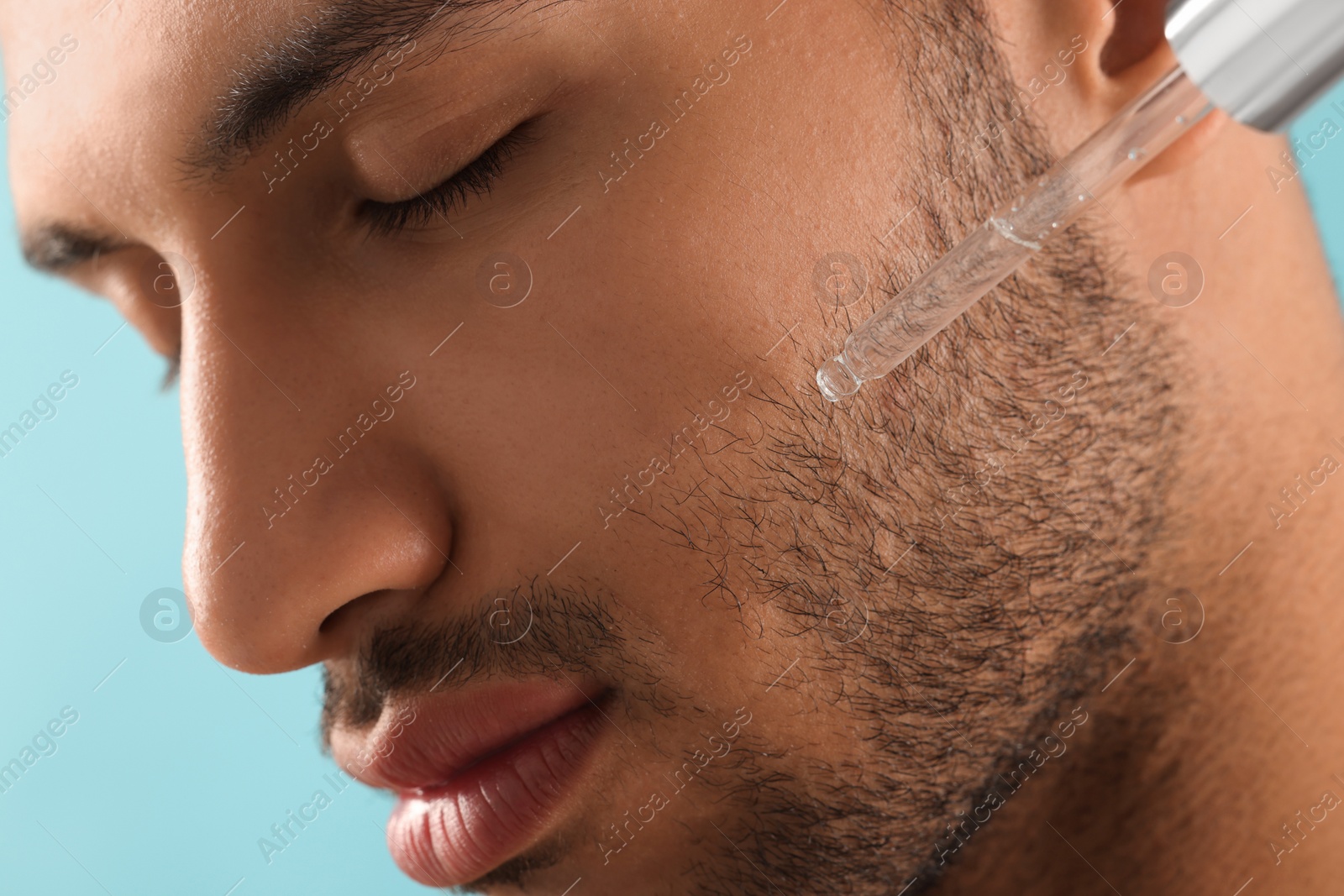 Photo of Handsome man applying cosmetic serum onto face, closeup