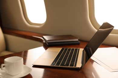 Photo of Laptop with notebooks and cup of coffee on table in airplane
