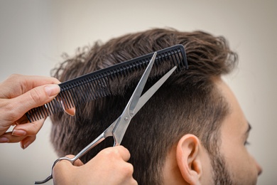 Barber making stylish haircut with professional scissors in beauty salon, closeup