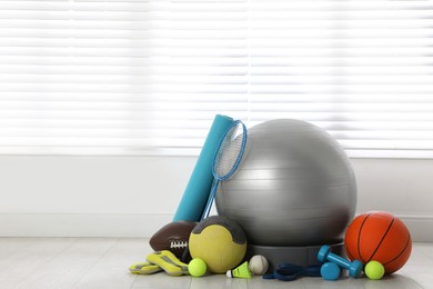 Set of different sports equipment on white floor indoors, space for text