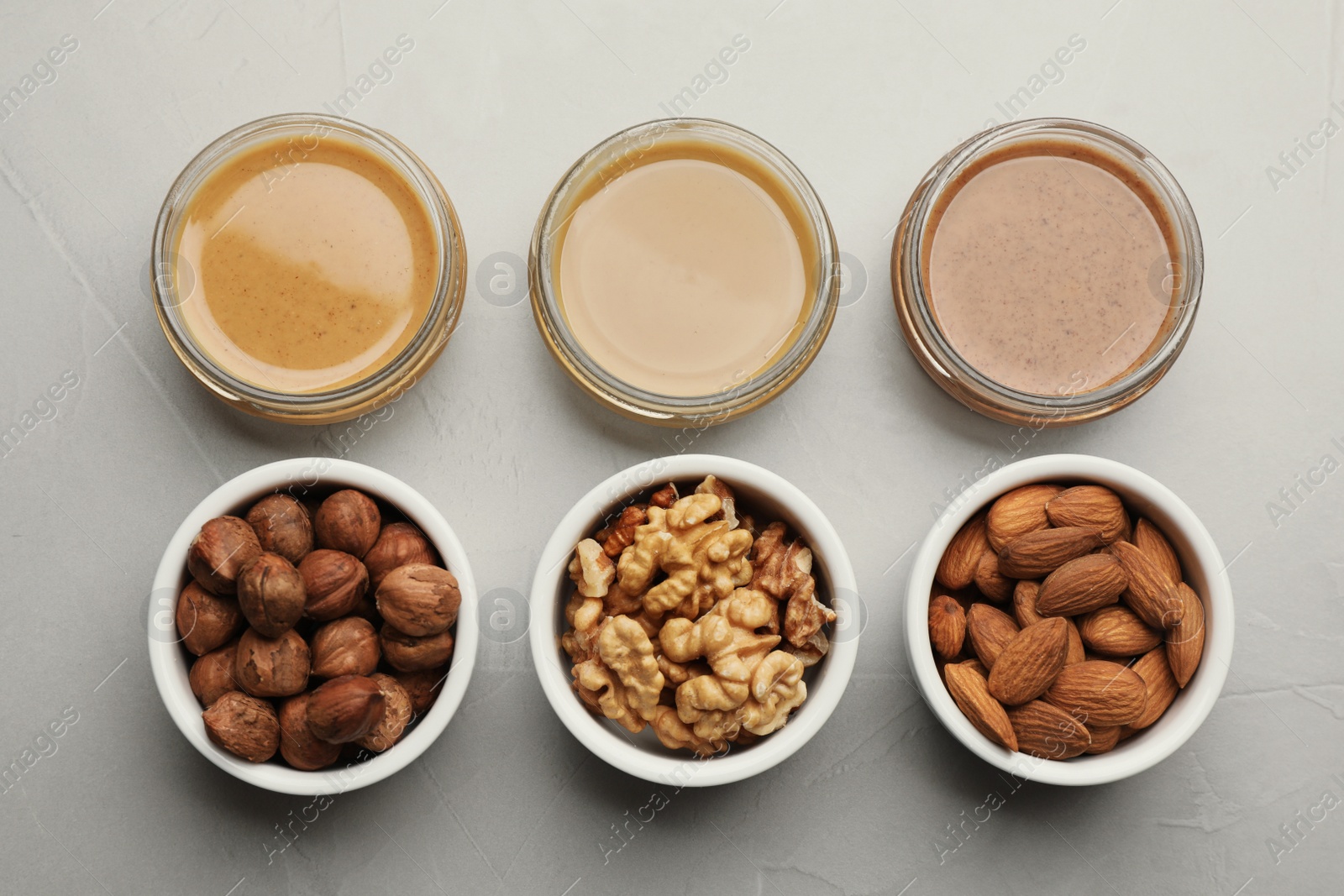 Photo of Different types of delicious nut butters and ingredients on grey table, flat lay