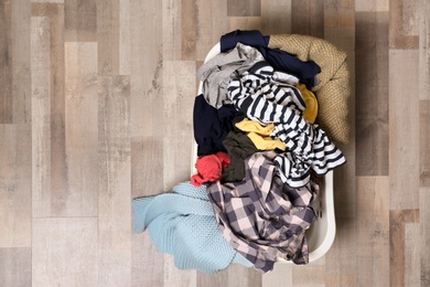 Photo of Laundry basket with dirty clothes on floor, top view. Space for text