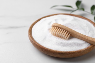 Photo of Bamboo toothbrush, green leaf and bowl of baking soda on white marble table, closeup. Space for text