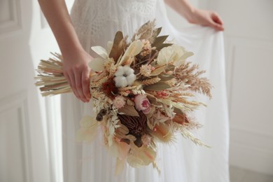 Bride holding beautiful dried flower bouquet at home, closeup