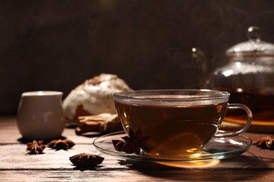 Glass cup of aromatic hot tea with anise stars on wooden table. Space for text