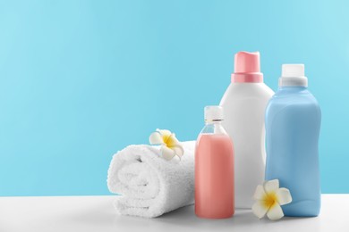Photo of Bottles of laundry detergents, towel and plumeria flowers on white table. Space for text