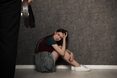 Man with belt standing in front of crying woman indoors, space for text. Stop sexual assault