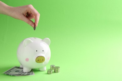 Photo of Financial savings. Woman putting coin into piggy bank on green background, closeup. Space for text