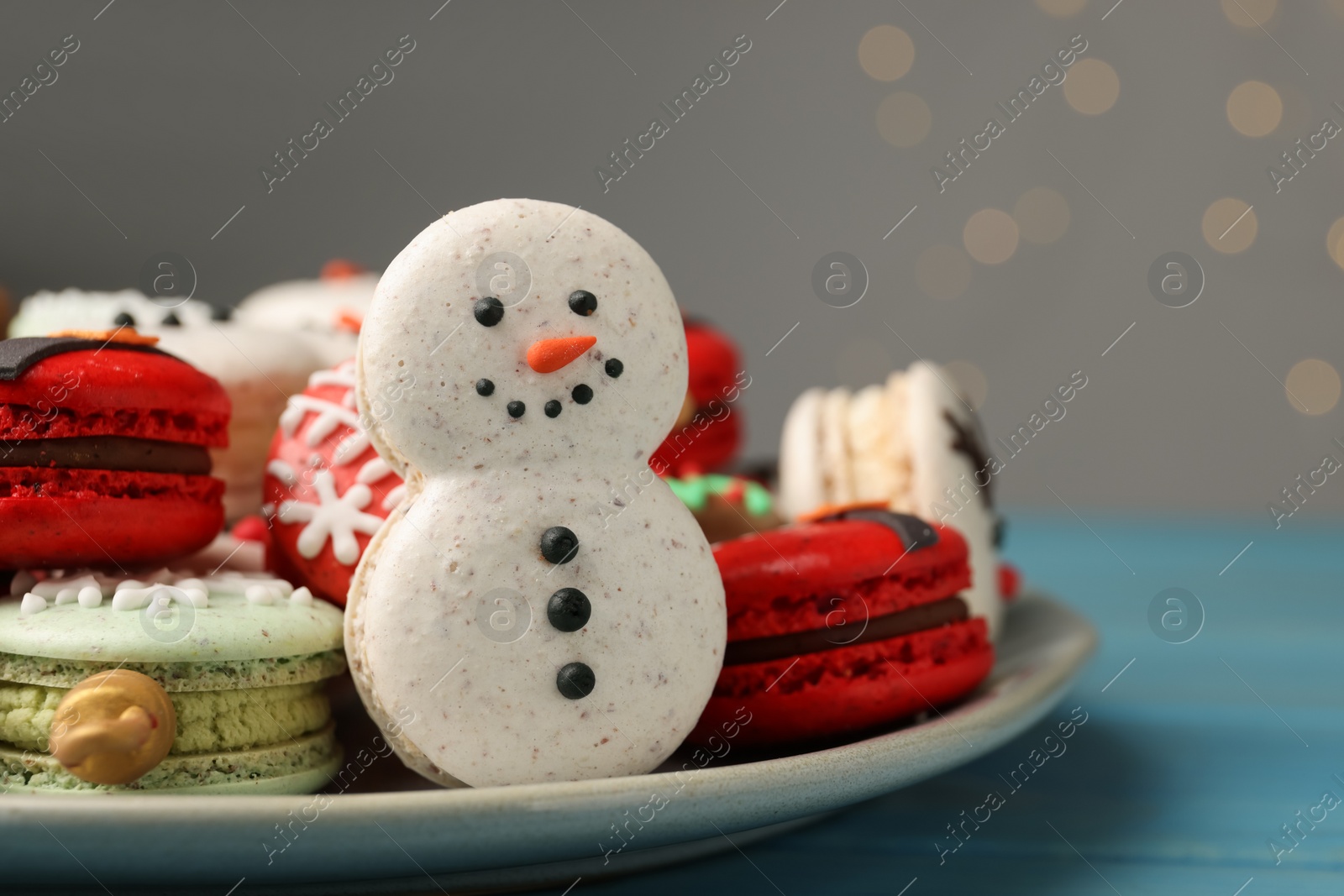 Photo of Beautifully decorated Christmas macarons on light blue wooden table against blurred festive lights, closeup. Space for text