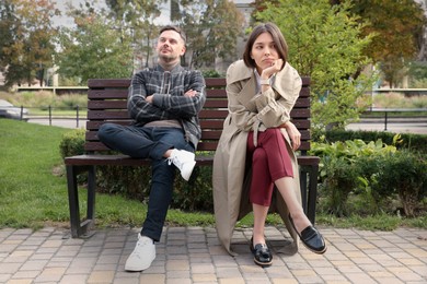 Photo of Bored woman sitting near her careless boyfriend on bench outdoors. Relationship problems