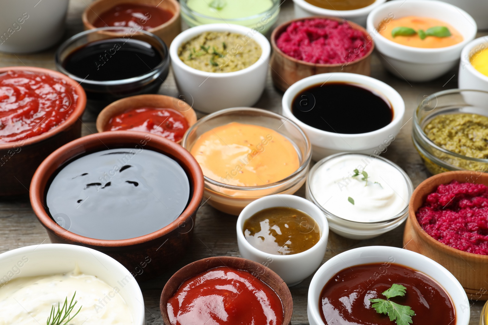 Photo of Many bowls with different sauces and herbs on wooden table