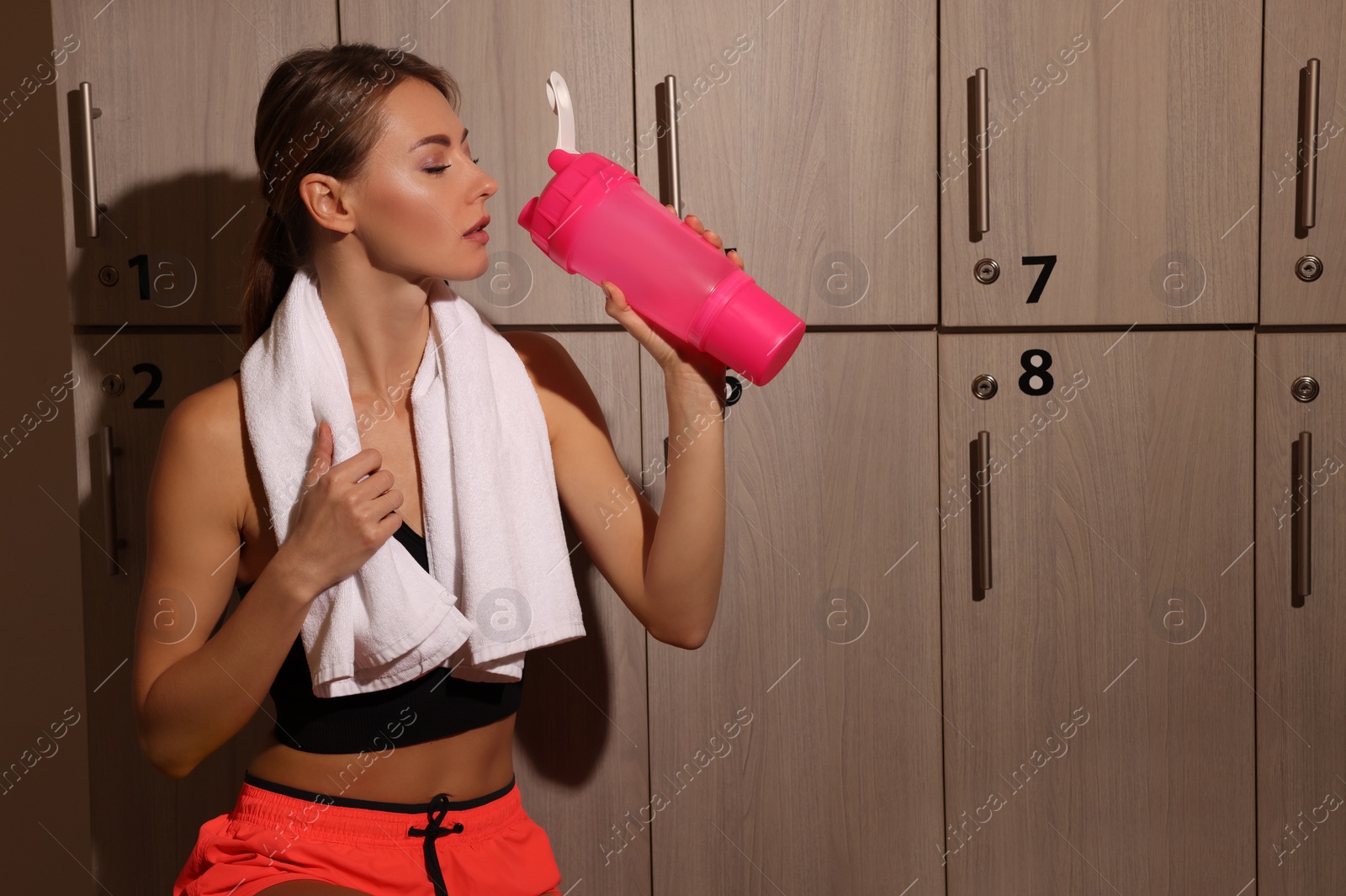 Photo of Beautiful woman drinking water in locker room
