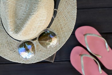 Stylish hat with sunglasses and flip flops on wooden floor, top view. Beach accessories