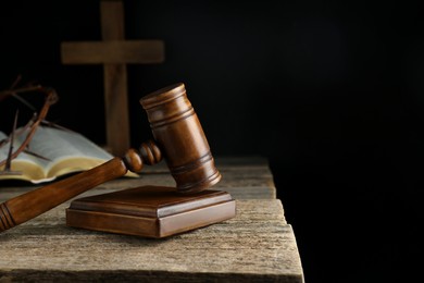 Photo of Judge gavel, bible, cross and crown of thorns on wooden table against black background. Space for text