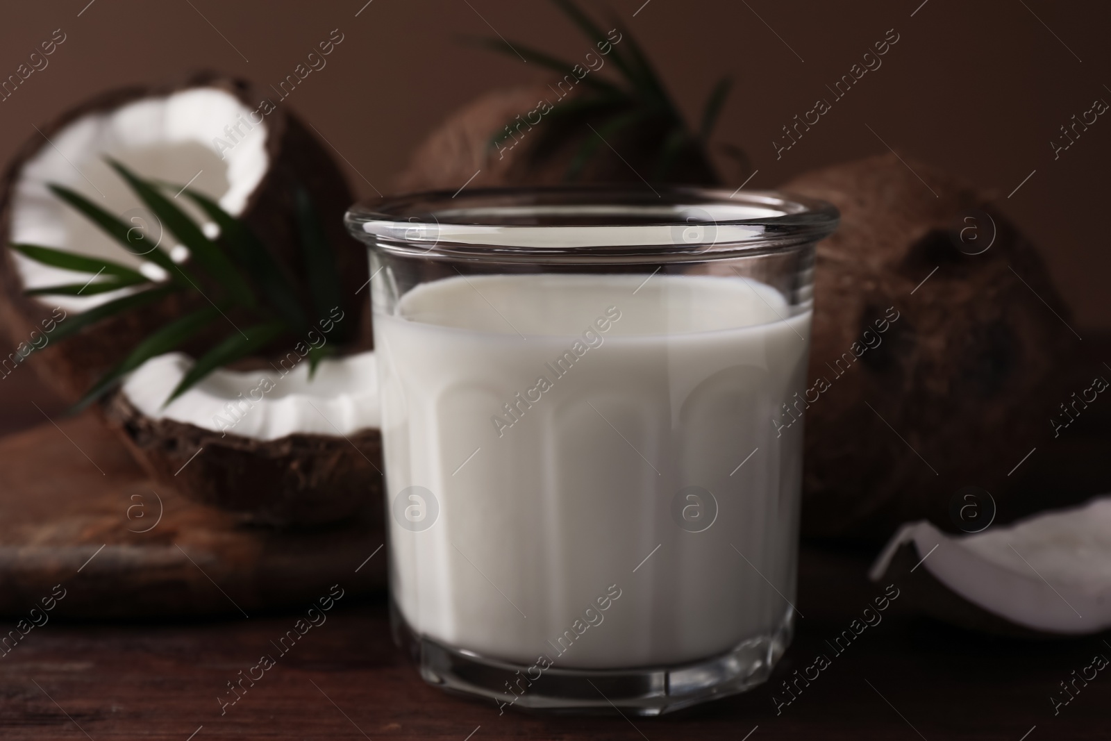 Photo of Glass of delicious vegan milk, coconut pieces and palm leaves on wooden table