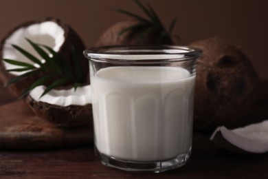 Photo of Glass of delicious vegan milk, coconut pieces and palm leaves on wooden table