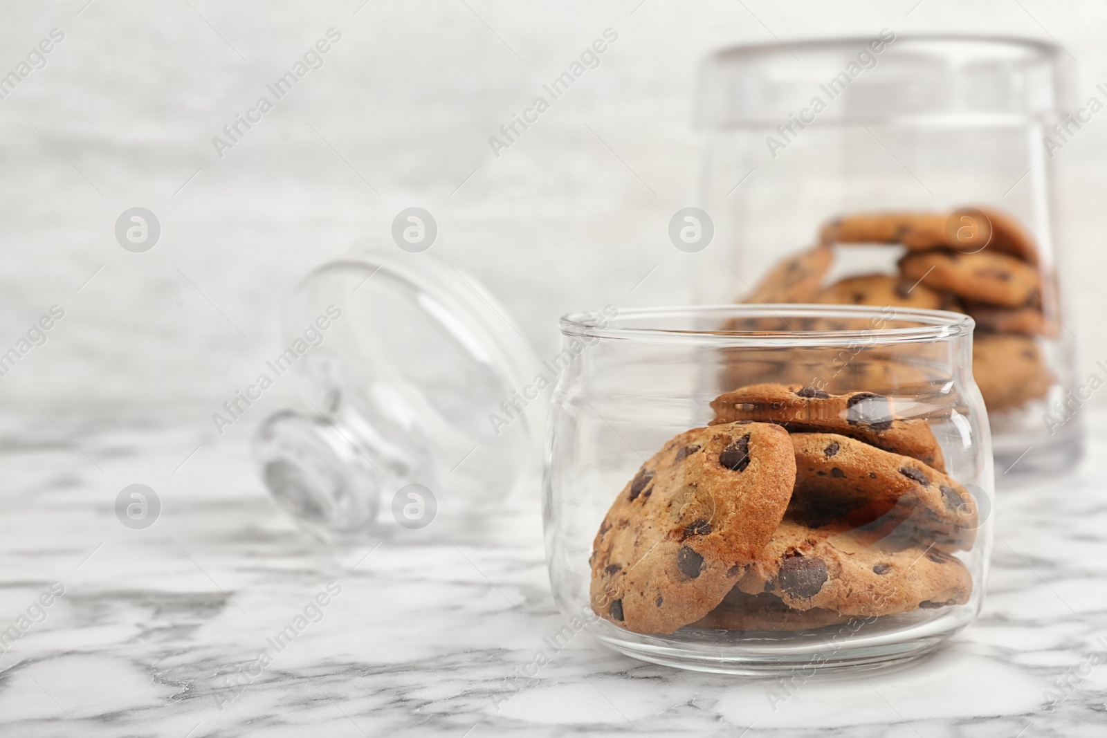 Photo of Jar with chocolate chip cookies on marble background, space for text