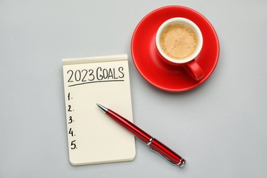 Photo of Making goals for 2023 new year. Notebook, pen and cup of coffee on light background, flat lay
