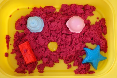 Photo of Bright kinetic sand and toys in yellow basin, top view