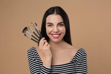 Photo of Happy woman with different makeup brushes on light brown background