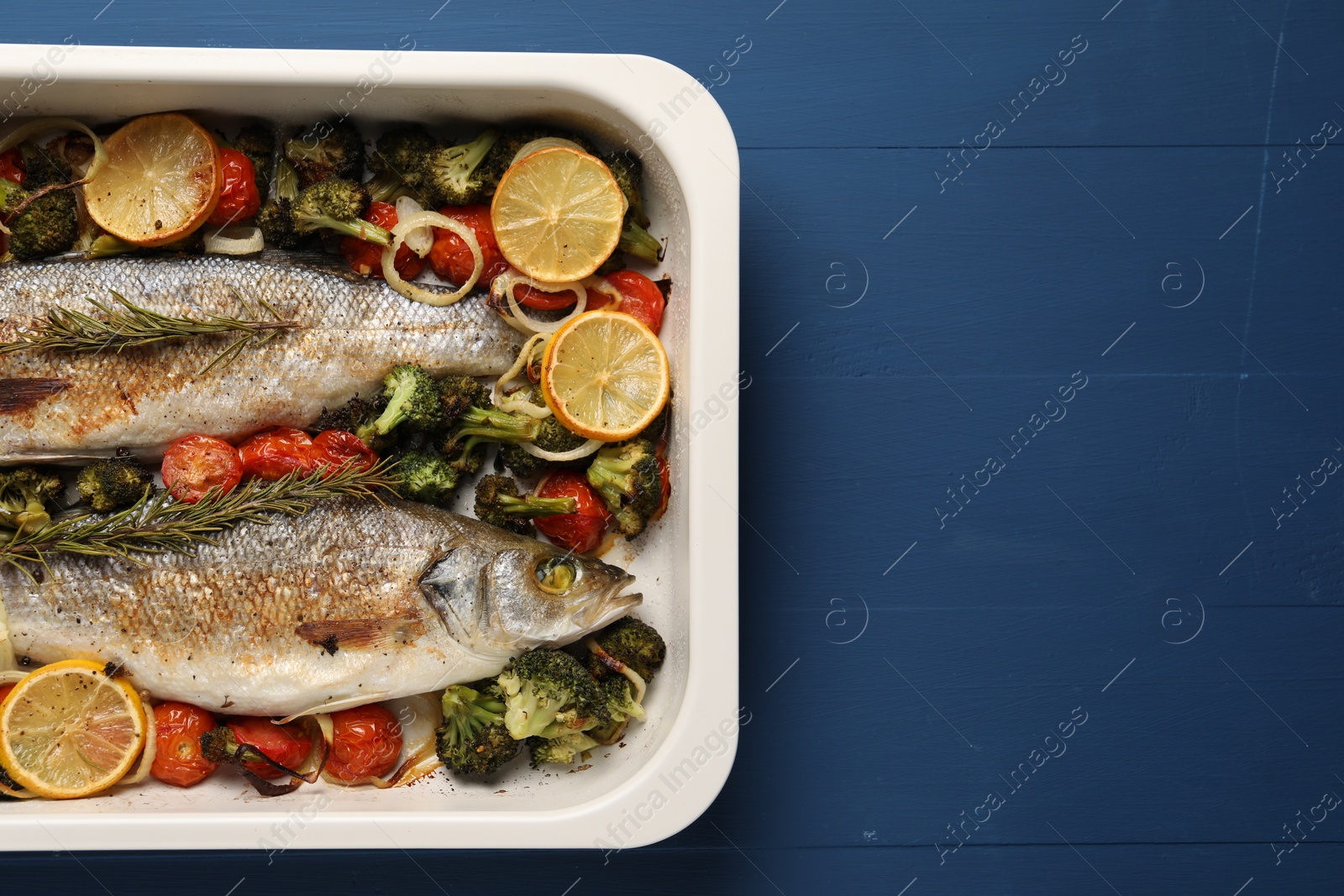 Photo of Delicious fish with vegetables and lemon in baking dish on blue wooden table, top view. Space for text