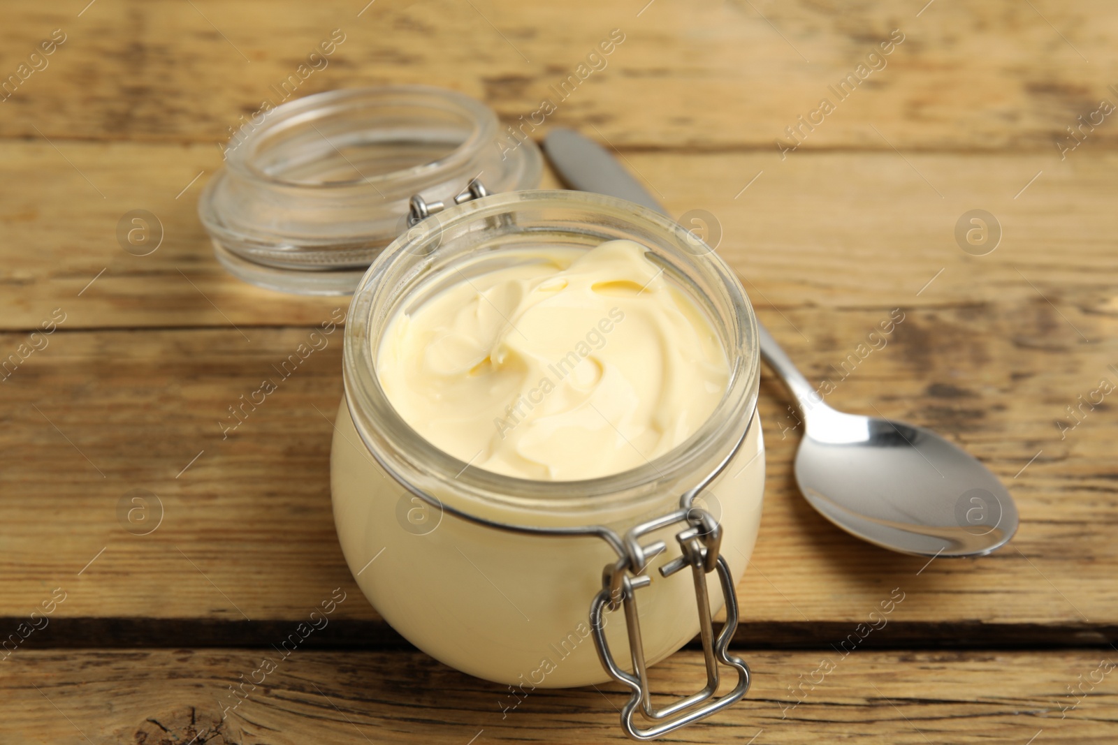 Photo of Jar of delicious mayonnaise and spoon on wooden table