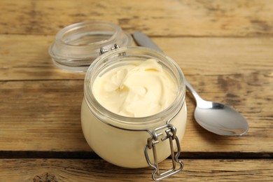 Jar of delicious mayonnaise and spoon on wooden table