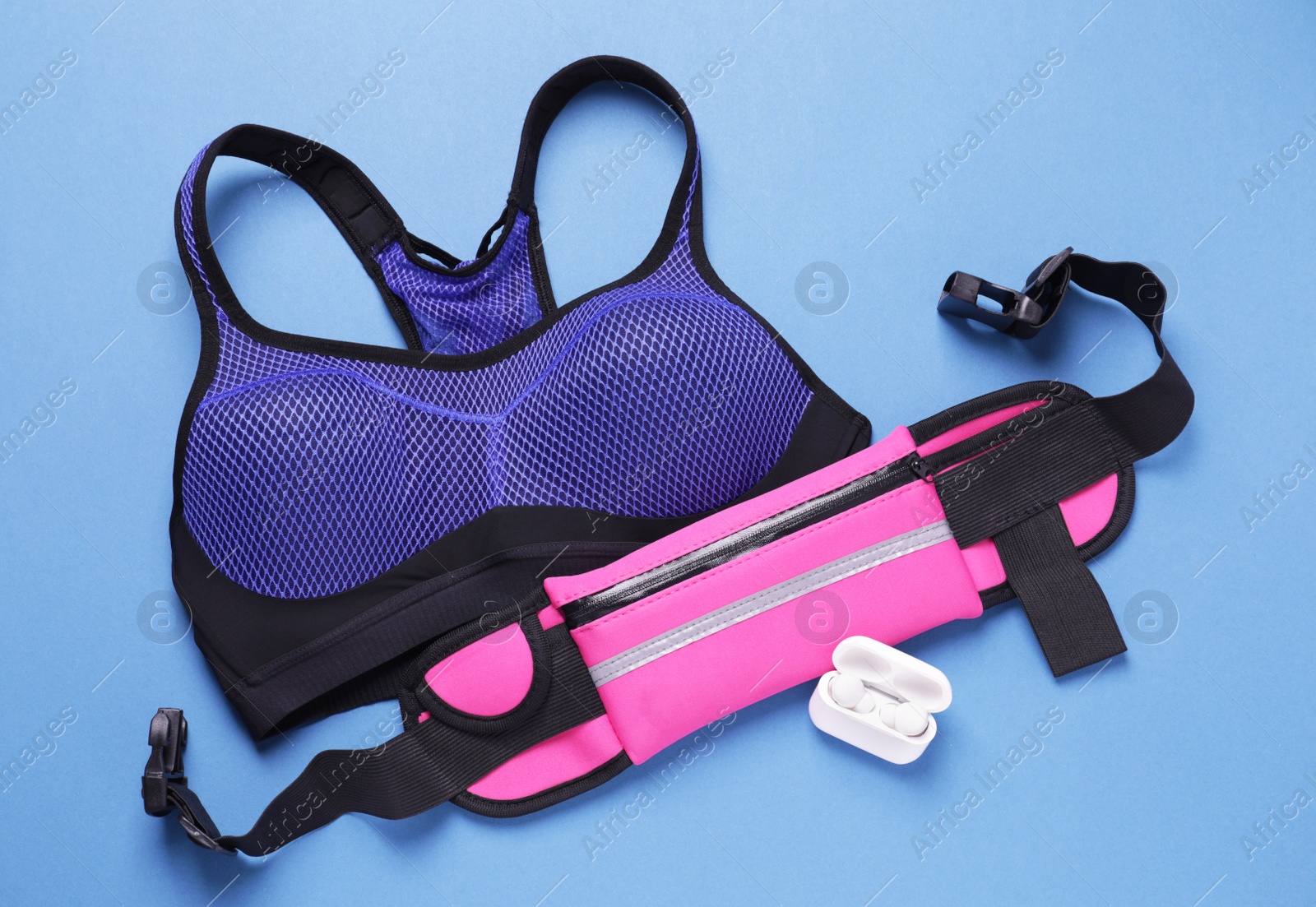 Photo of Stylish pink waist bag, earphones and sportswear on light blue background, flat lay