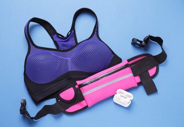 Photo of Stylish pink waist bag, earphones and sportswear on light blue background, flat lay