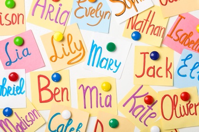 Photo of Colorful paper sheets with written different baby names on white background, flat lay