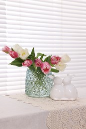 Photo of Easter decorations. Bouquet of tulips in vase and bunny figures on white table at home