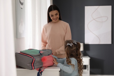 Young mother helping her little child get ready for school in bedroom