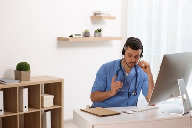 Doctor with headset consulting patient online at desk in clinic, space for text. Health service hotline