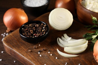 Whole and cut onion with spices on wooden table, closeup