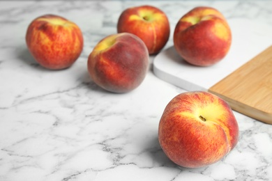 Photo of Fresh peaches and wooden board on marble table, space for text