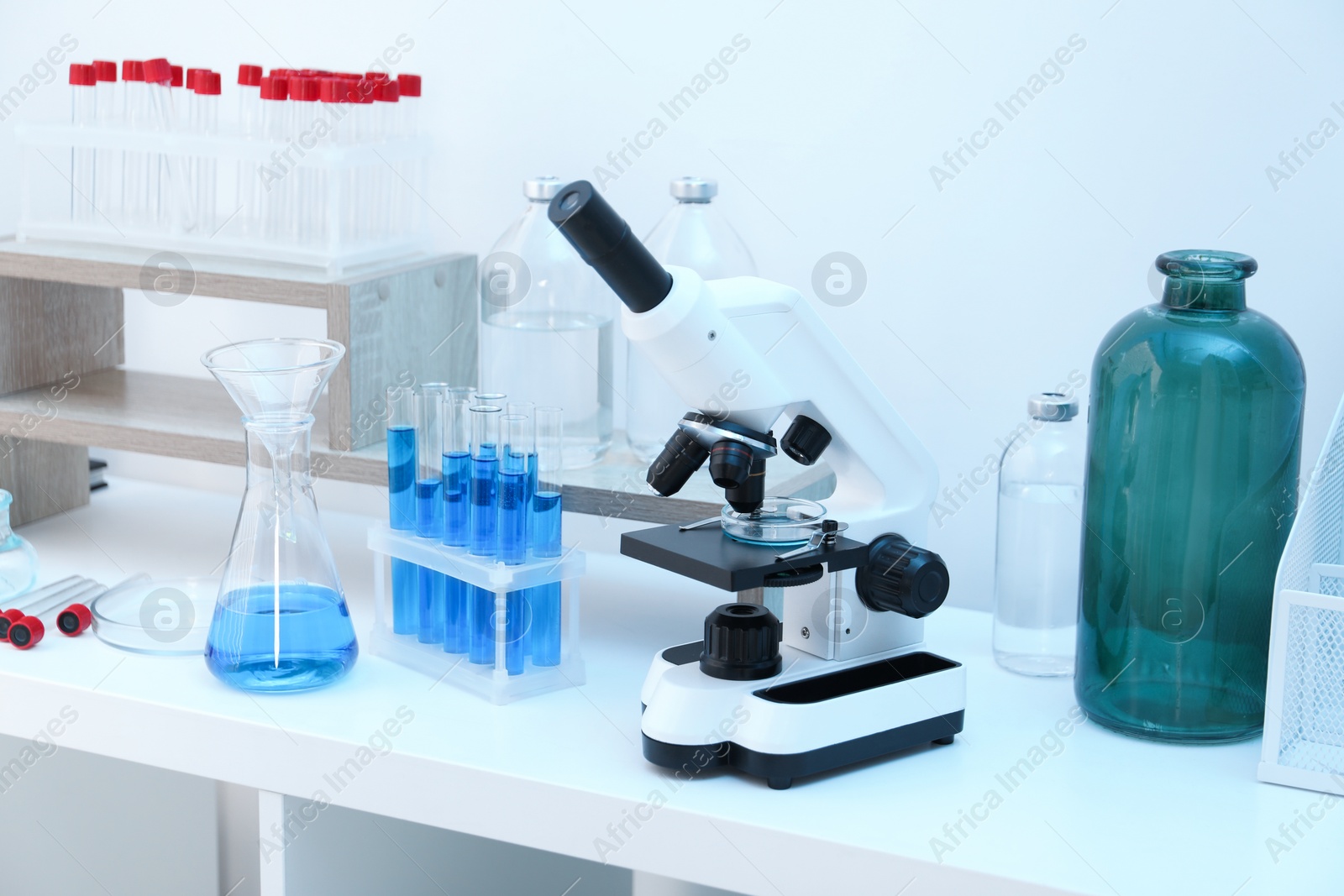 Photo of Laboratory analysis. Different glassware with blue liquid and microscope on white table indoors