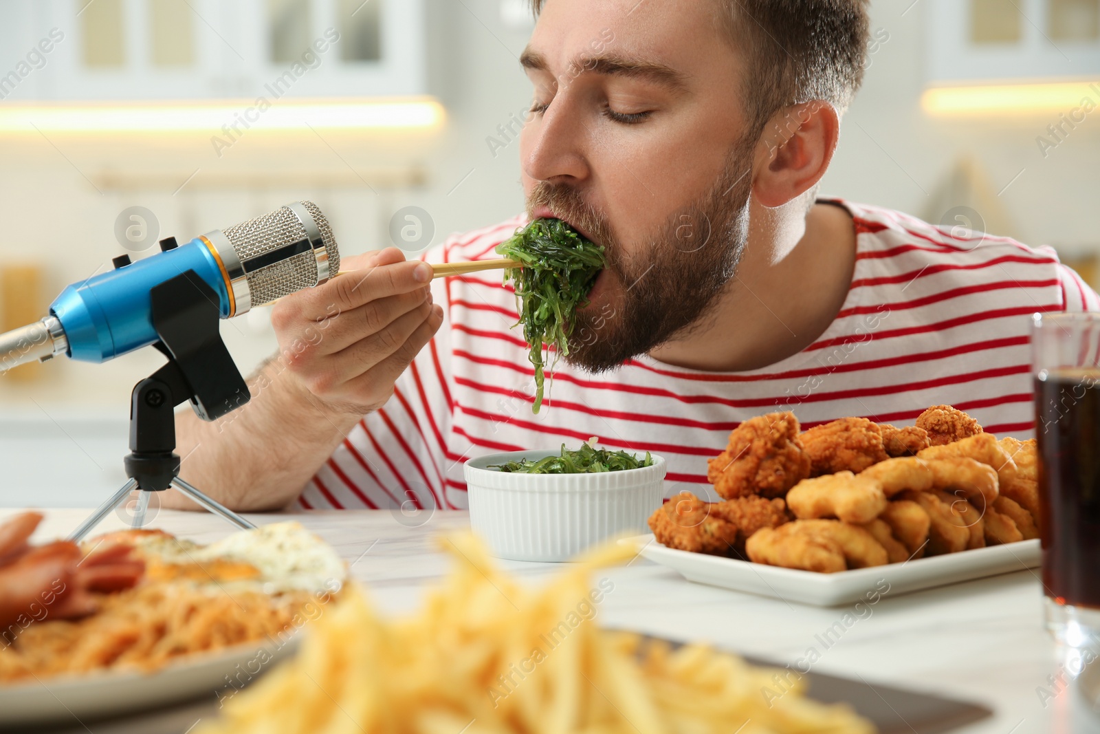 Photo of Food blogger eating near microphone at table in kitchen, closeup. Mukbang vlog