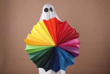 Photo of Person in ghost costume with rainbow umbrella on dark beige background