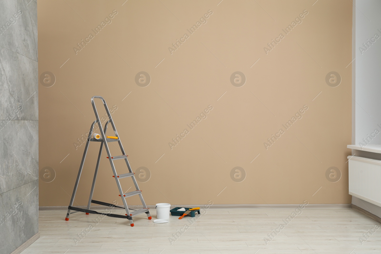 Photo of Metallic folding ladder and painting tools near beige wall indoors, space for text