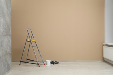 Photo of Metallic folding ladder and painting tools near beige wall indoors, space for text