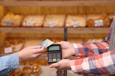 Photo of Woman using credit card for terminal payment in bakery, closeup
