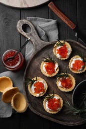 Photo of Delicious tartlets with red caviar and cream cheese served on wooden table, flat lay