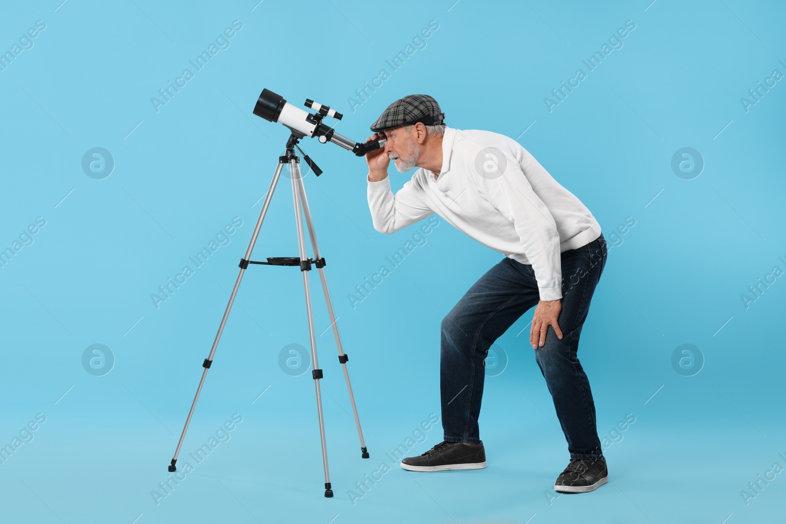 Photo of Senior astronomer looking at stars through telescope on light blue background