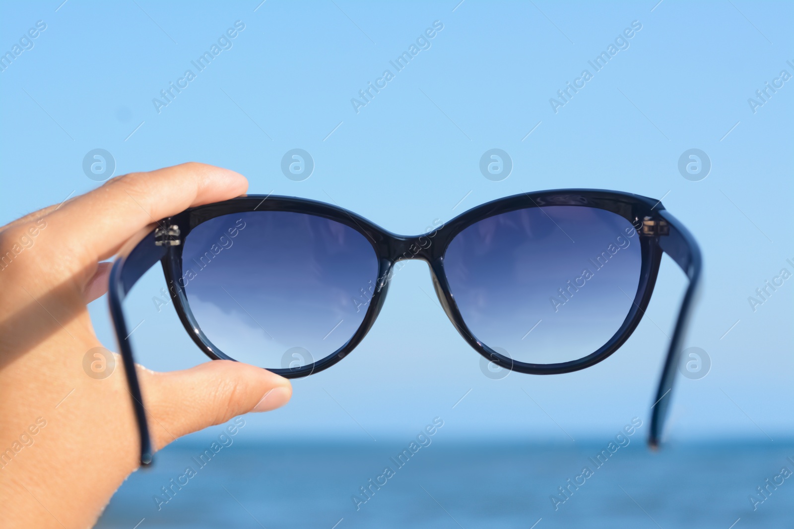 Photo of Woman holding stylish sunglasses near sea, closeup