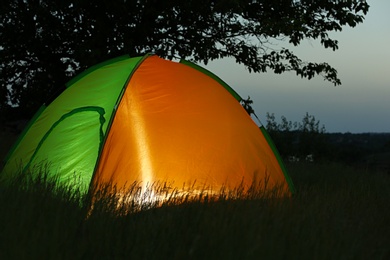 Photo of Modern tent lit from inside in wilderness at night. Overnight camping