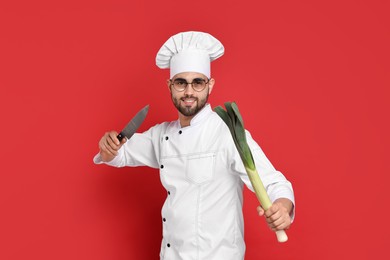 Photo of Professional chef with leek and knife having fun on red background